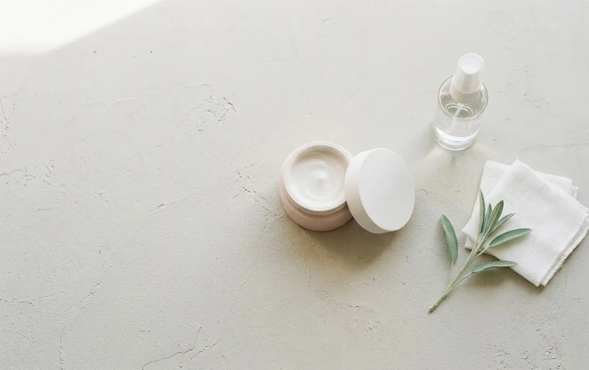 Routine minimalista per dermatite periorale: crema lenitiva, acqua termale e garze di cotone su fondo chiaro