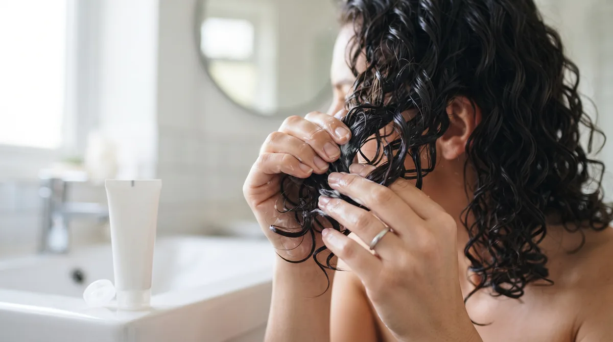 Mani che modellano con una crema bianca dei ricci naturali definiti, accanto a un tubetto senza etichetta
