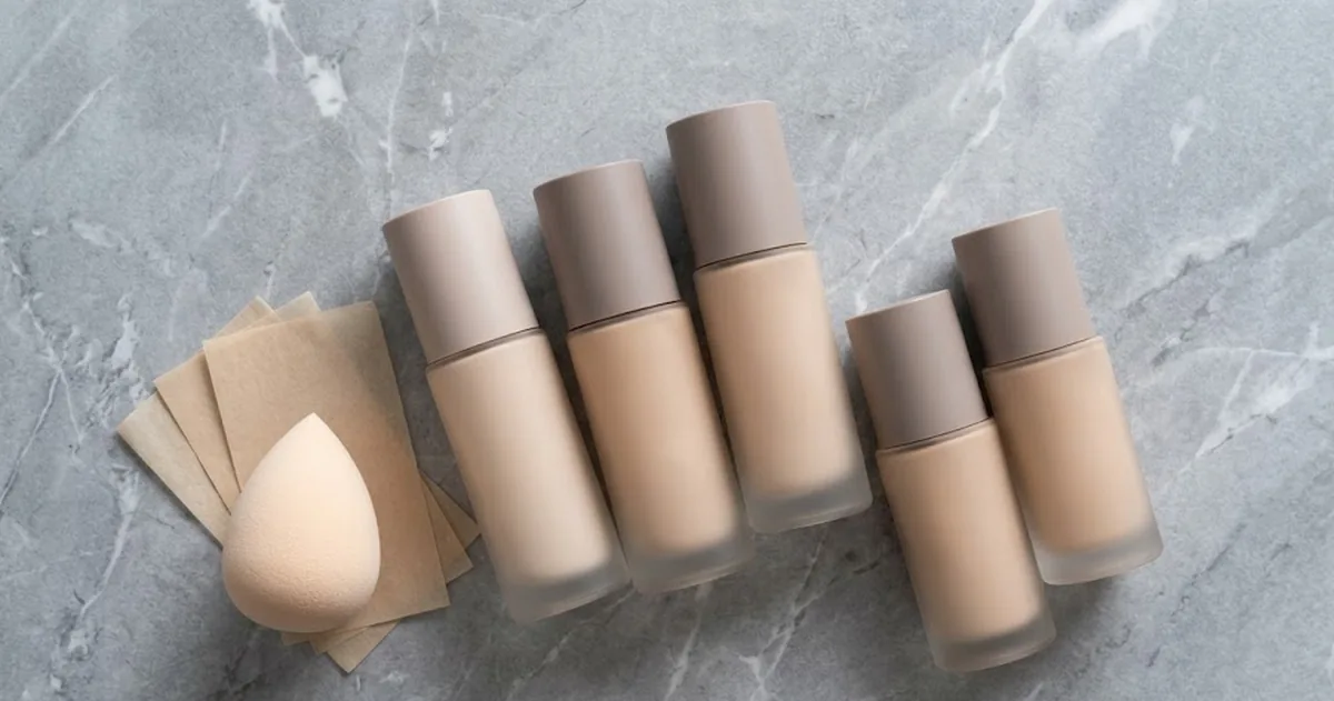Cinque fondotinta per pelle grassa a confronto con finish opaco su sfondo neutro, pennelli e spugnette makeup