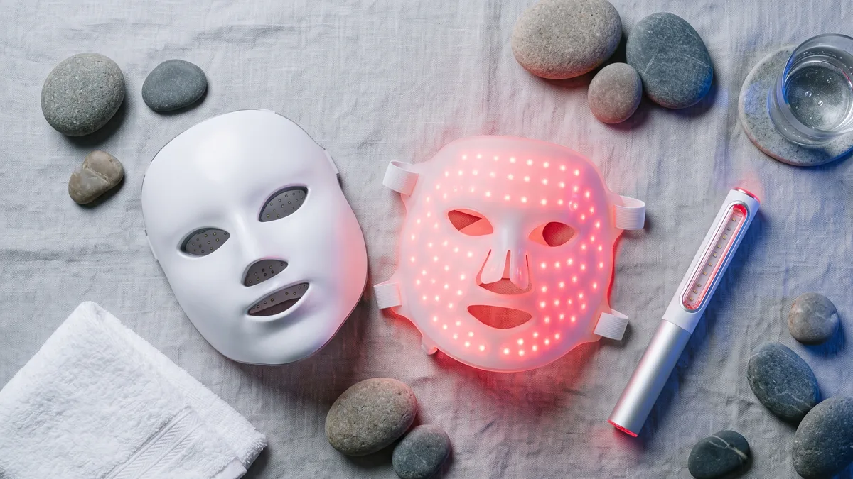 Maschera LED viso accesa con luce rossa appoggiata su un ripiano accanto a occhiali protettivi e prodotti skincare