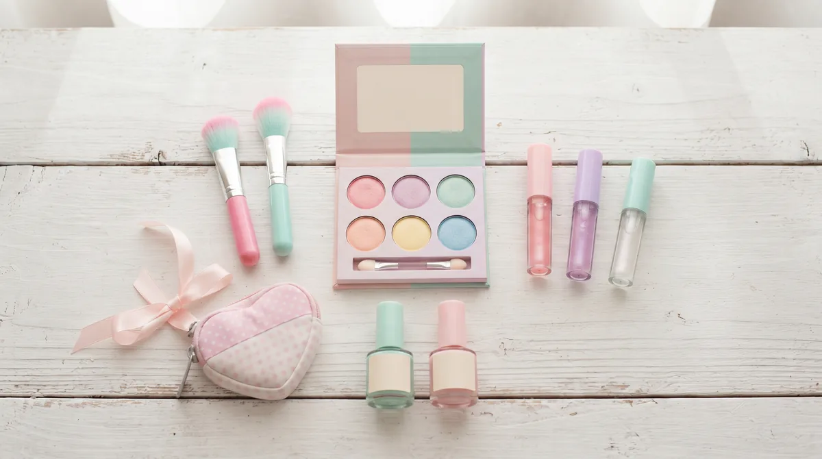 Set trucchi per bambina in colori pastello: palette di ombretti, lucidalabbra, pennellini e smalti su un tavolo bianco