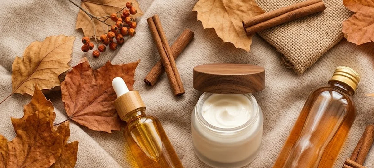 Flat lay di prodotti skincare invernali su superficie in lino beige con elementi autunnali naturali